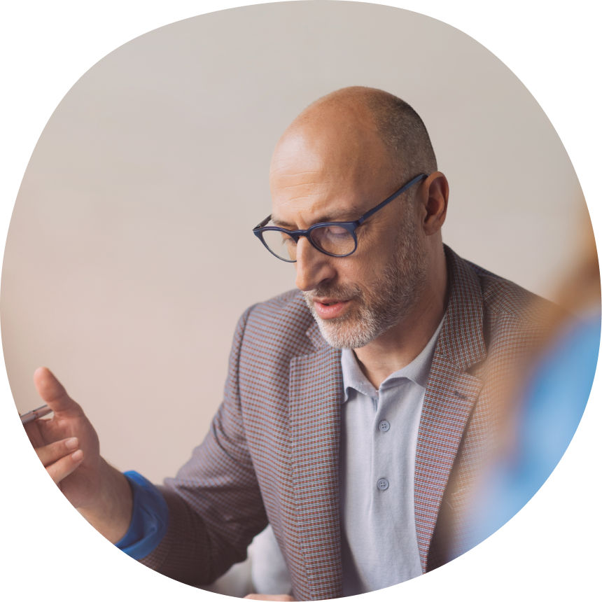 Male therapist with glasses and beard in professional blazer gesturing expressively while speaking to client, with open book in hand, conveying warmth and engagement in therapeutic conversation